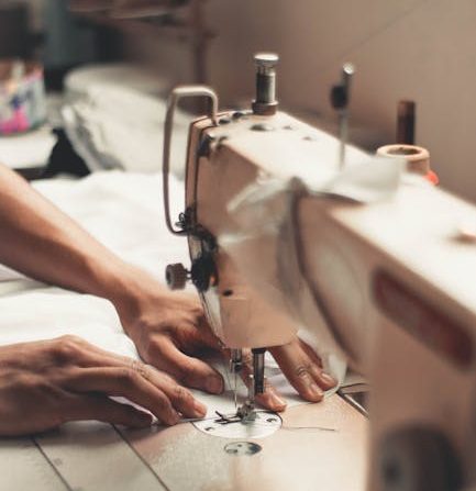 Close-up of hands using a sewing machine, depicting craftsmanship and textiles indoors.