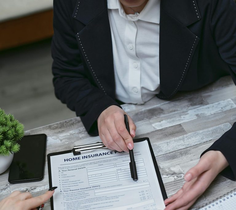 An agent and clients discussing paperwork for home insurance at a meeting table.
